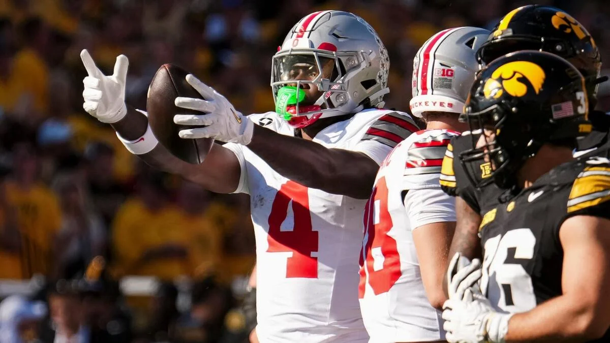 Ohio State player in white jersey extends his arms beside teammates during a game against Iowa.