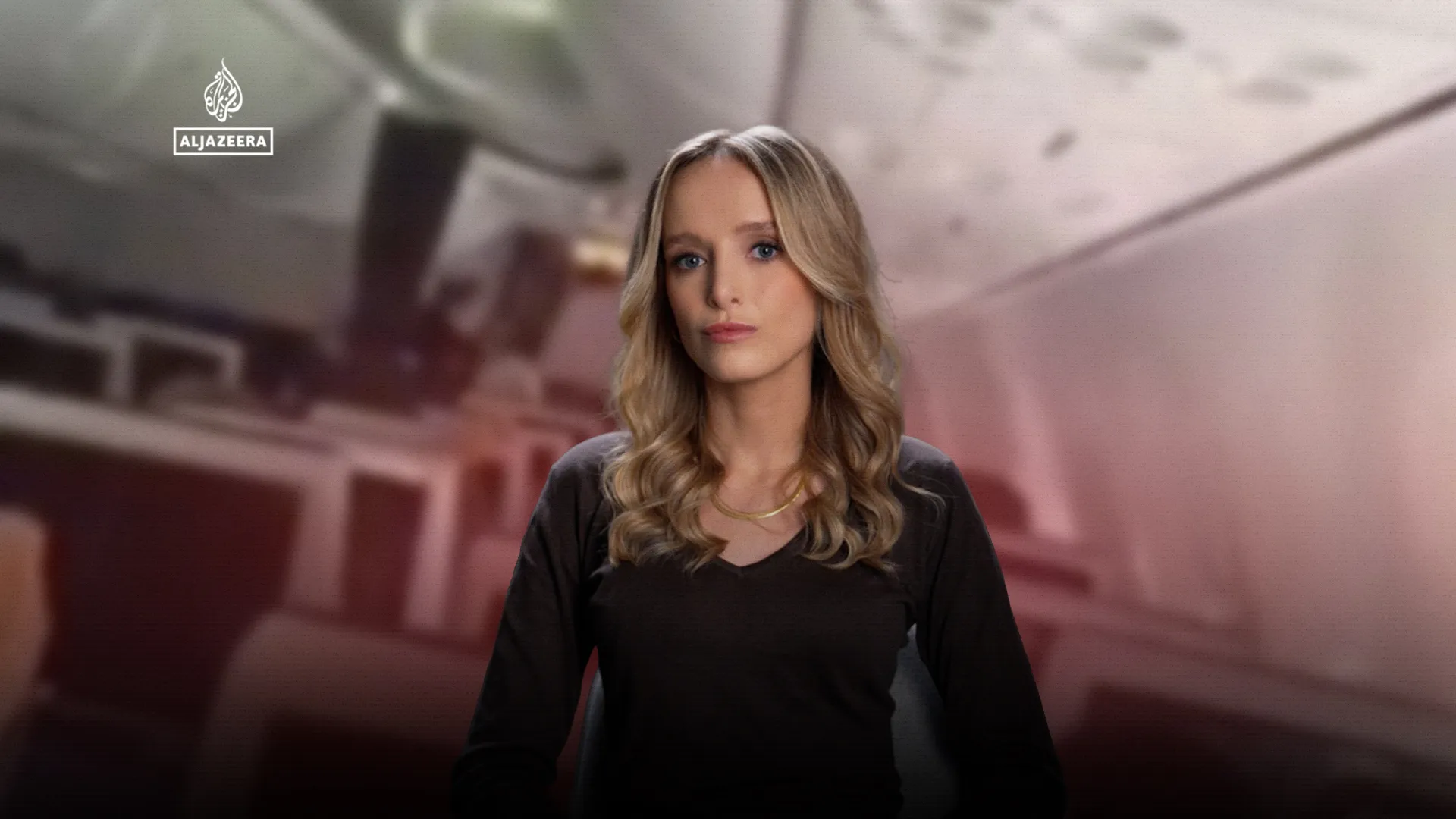Blonde woman in a black top sits facing the camera against a blurred pink-toned background, with an Al Jazeera logo.