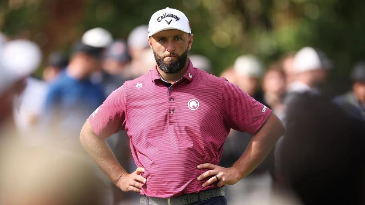 A golfer in a white cap and burgundy shirt stands with hands on hips amid a crowd.