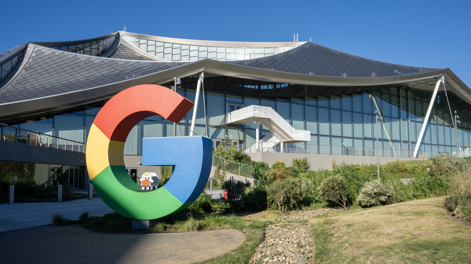 Large multicolored Google G sculpture stands outside a modern glass building beneath a clear blue sky.