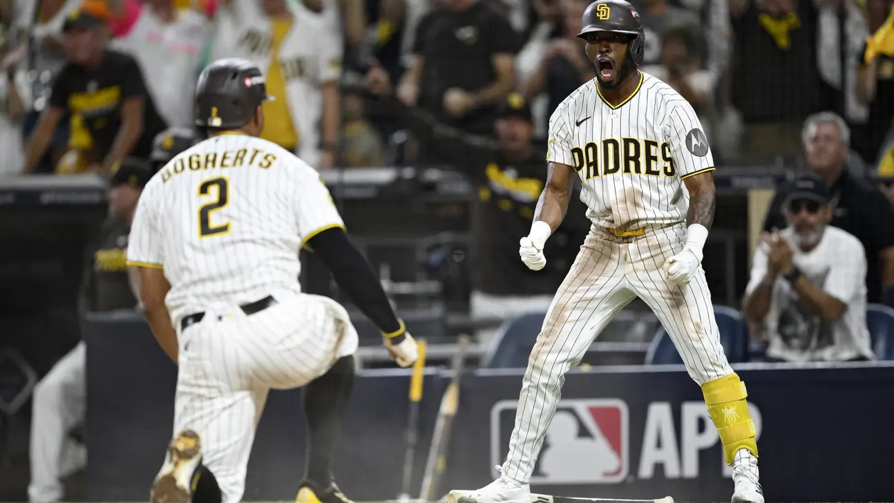 Padres player celebrates beside a teammate in a white pinstriped uniform on the field.