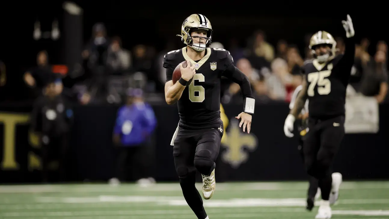 A Saints player wearing number 6 runs with the football as a teammate follows behind.