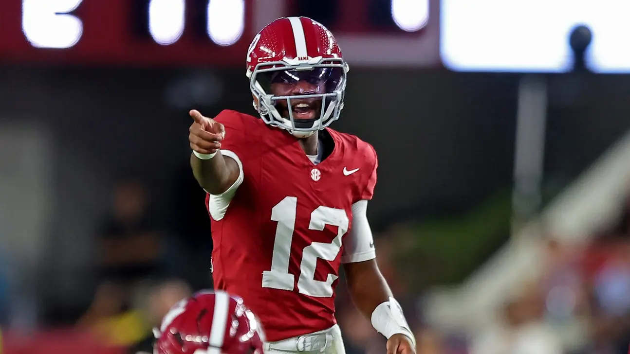 Alabama player in a red number 12 uniform points forward on the football field.