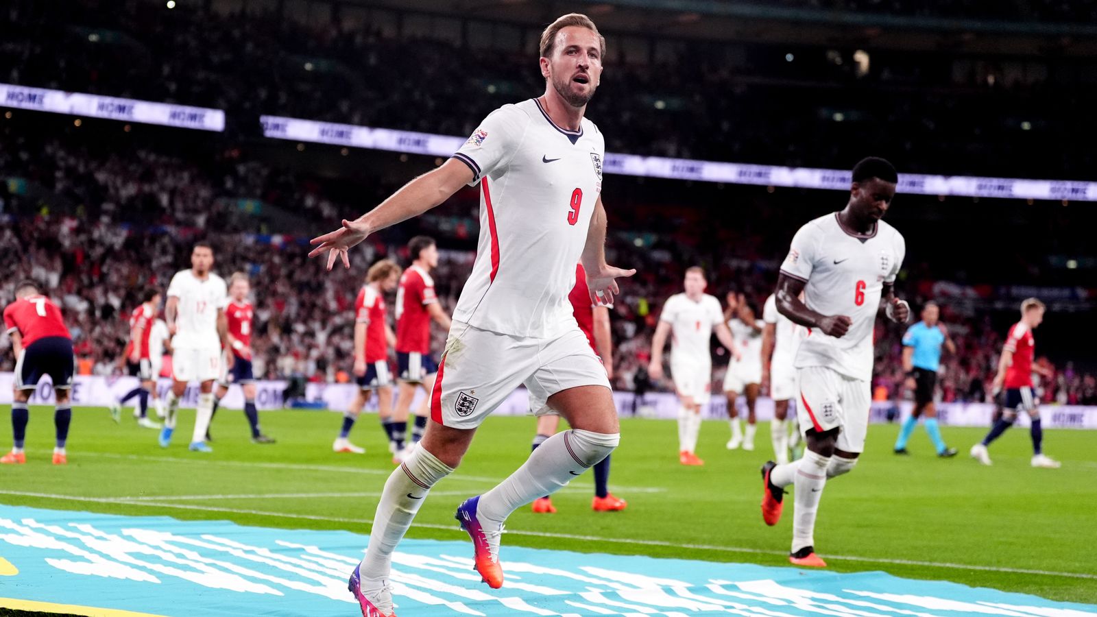 England players in white celebrate on the pitch as a forward runs with arms outstretched.