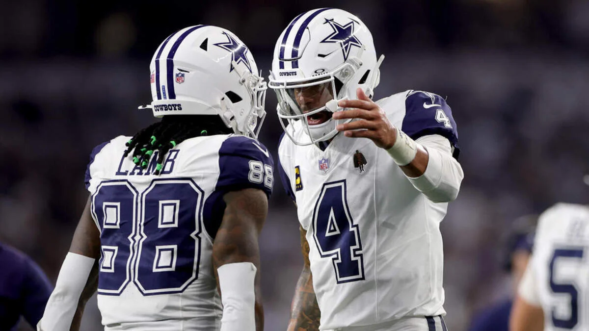 Two Dallas Cowboys players in white uniforms and helmets celebrate together on the field.