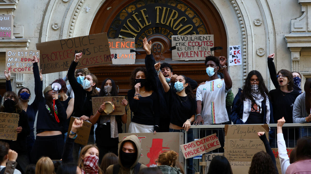 Masked demonstrators hold signs and raise fists outside a building entrance during a protest.