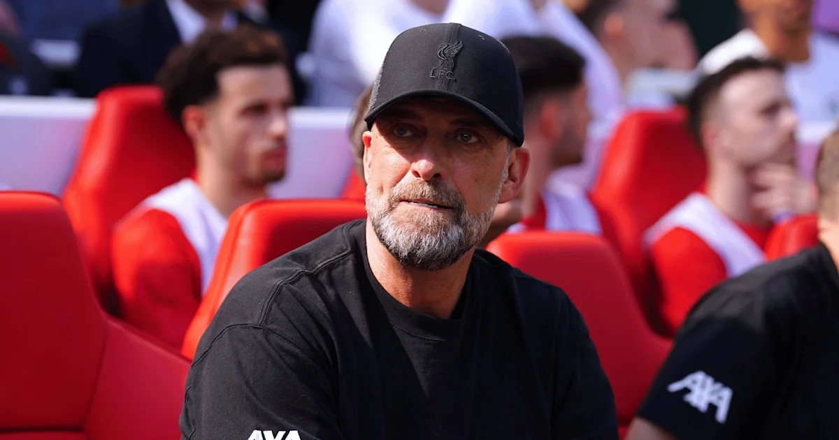A bearded man in a black cap and shirt sits among red stadium seats.