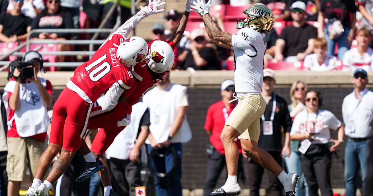 Louisville defenders in red leap toward a Wake Forest player in white during a football game.