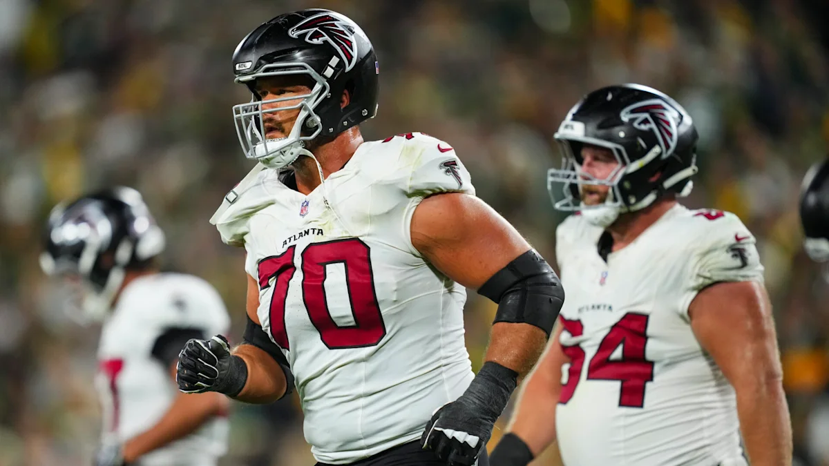 Atlanta Falcons players in white uniforms jog on the field, led by number 70.