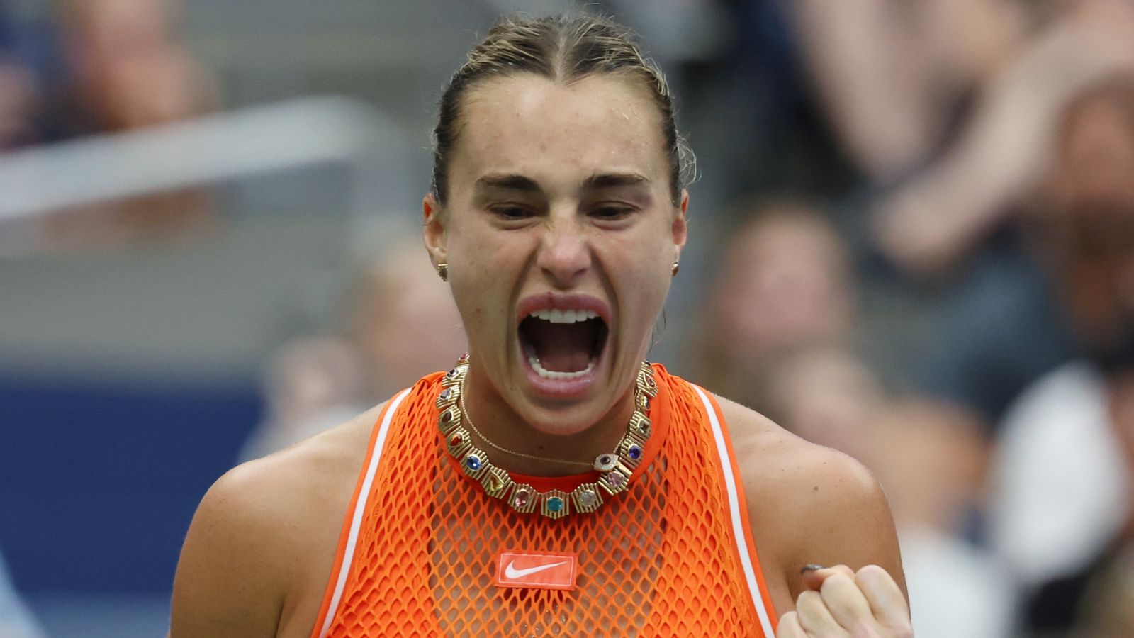 A tennis player in an orange top shouts with a clenched fist raised.
