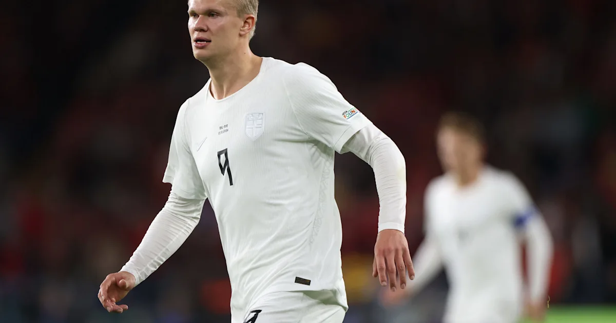 A footballer in a white number nine jersey runs forward, with another player blurred in the background.