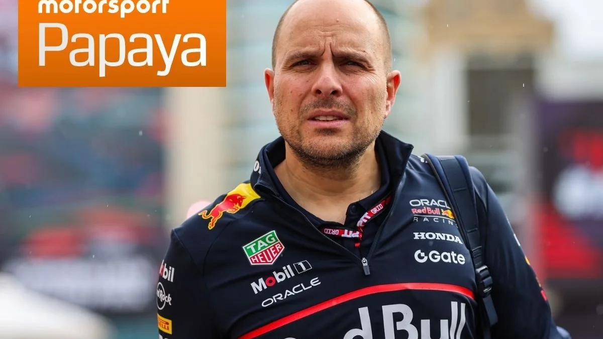 Bald man in a Red Bull Racing jacket stands outdoors, with an orange motorsport Papaya graphic at upper left.