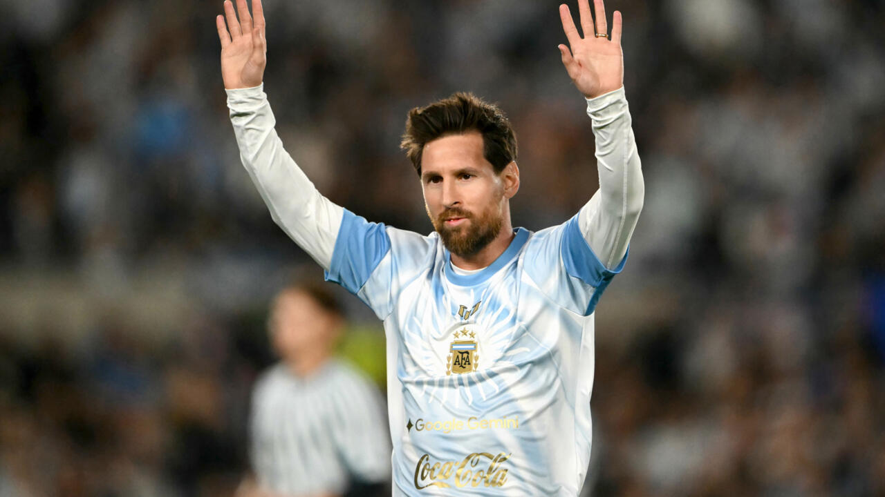 A footballer in Argentina’s sky blue and white jersey raises both hands before a blurred crowd.