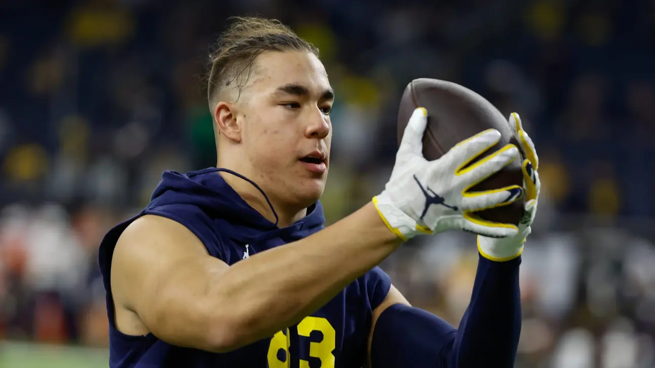 Football player in a navy sleeveless jersey and gloves holds a football during warmups.