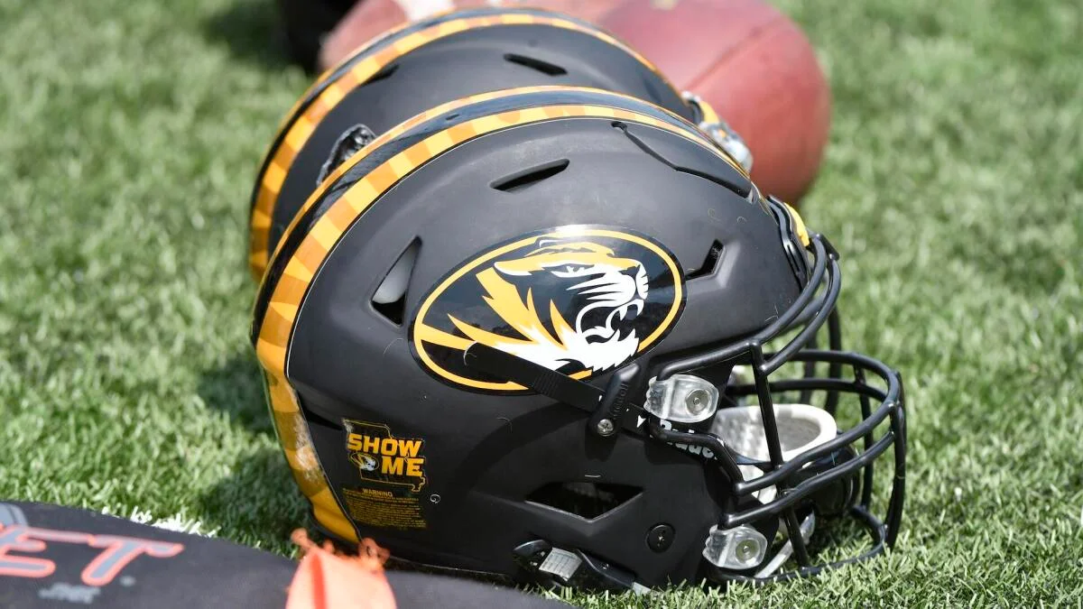 Black and gold Missouri Tigers football helmet resting on artificial turf beside a football.