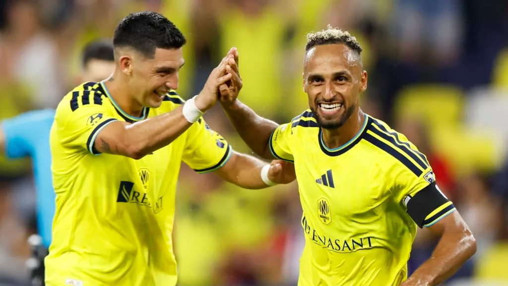 Two soccer players in yellow jerseys smile and high-five on the field.