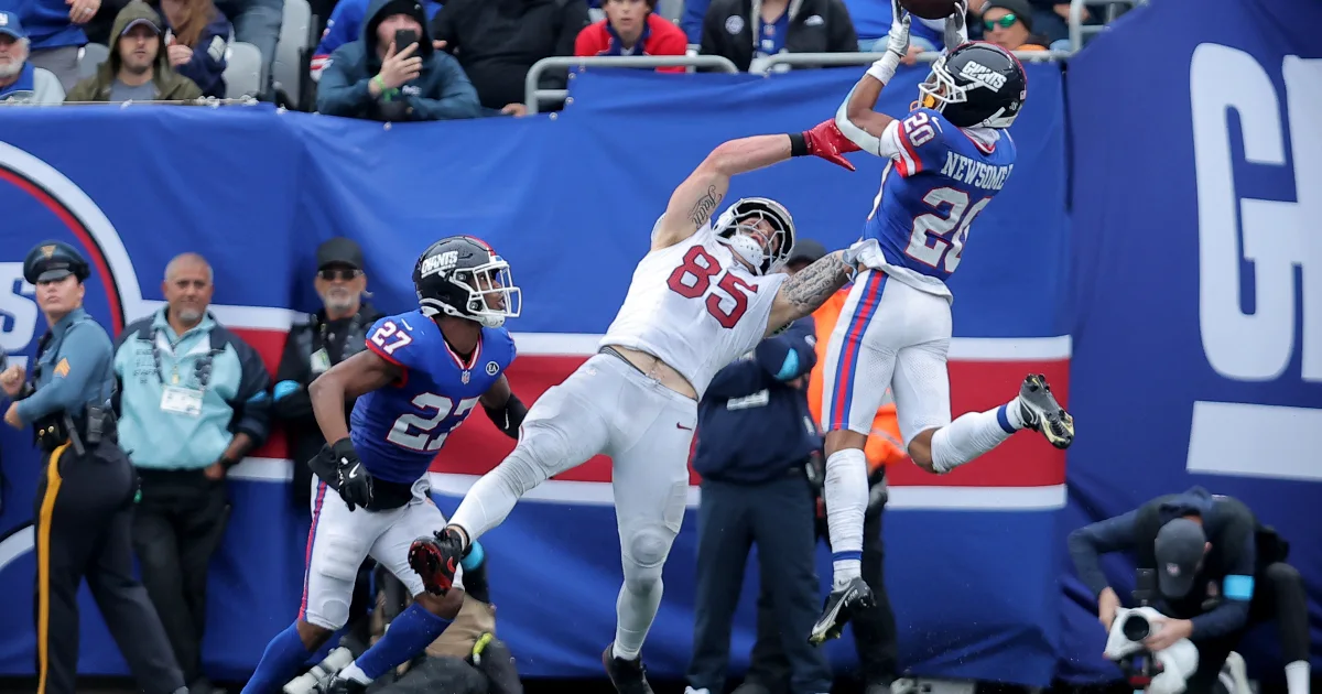 Giants defender leaps to contest a pass as a Cardinals player watches during an NFL game.