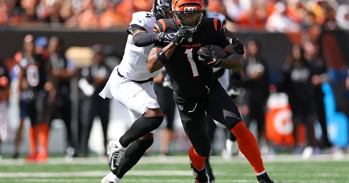 A Bengals player in a black uniform runs with the ball as a defender in white reaches toward him.