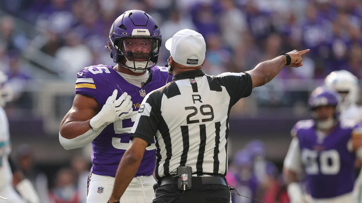 A Minnesota Vikings player gestures toward his chest as a referee points across the football field.