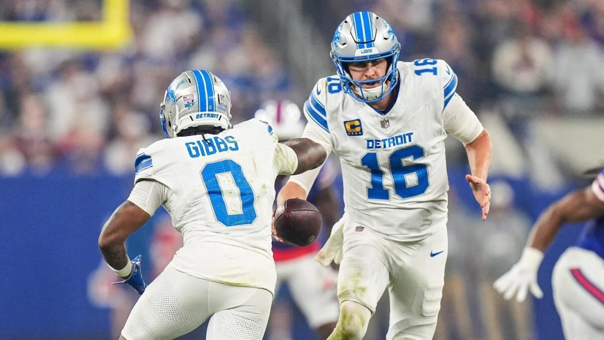 Detroit Lions players in white uniforms exchange the football during an NFL game.
