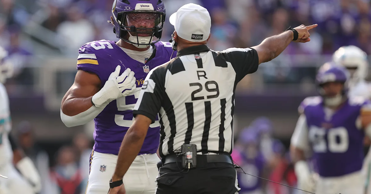 A referee signals with one arm as a Vikings player stands beside him during a game.