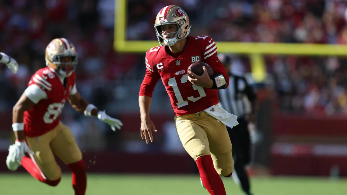 A San Francisco 49ers player runs with the football as a teammate follows on the field.
