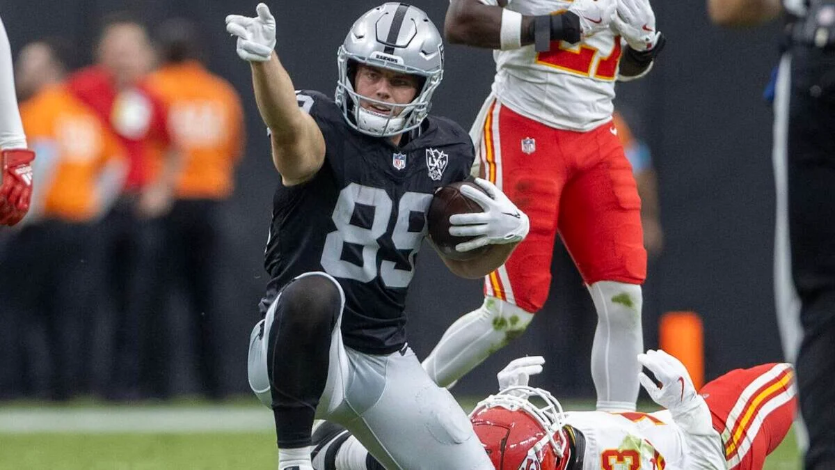 Raiders player in black uniform carries the ball past a fallen Chiefs player.
