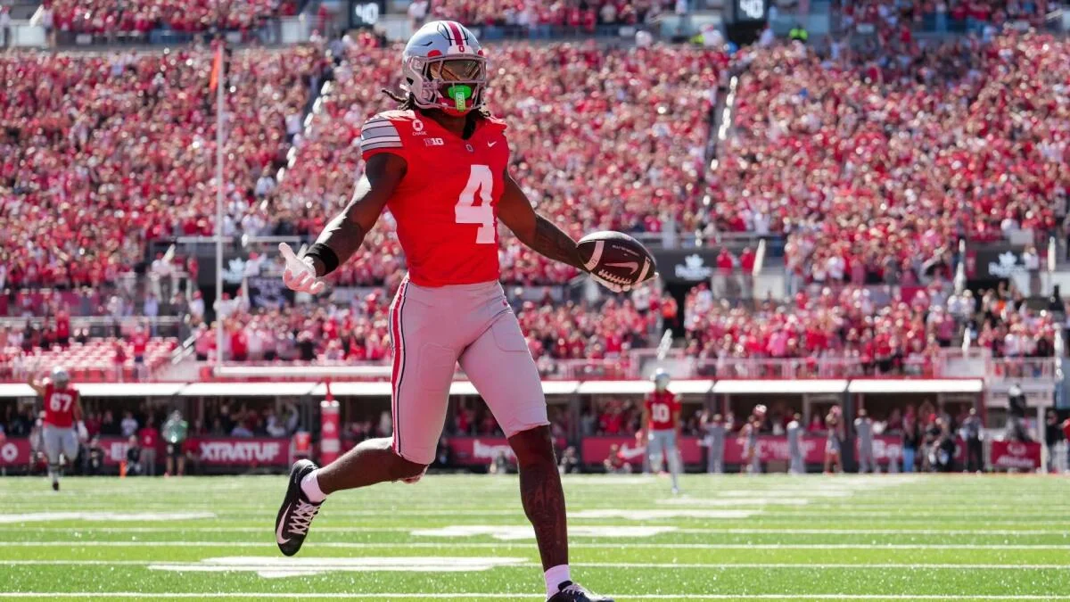 Ohio State player in a red number 4 uniform runs with a football during a game.