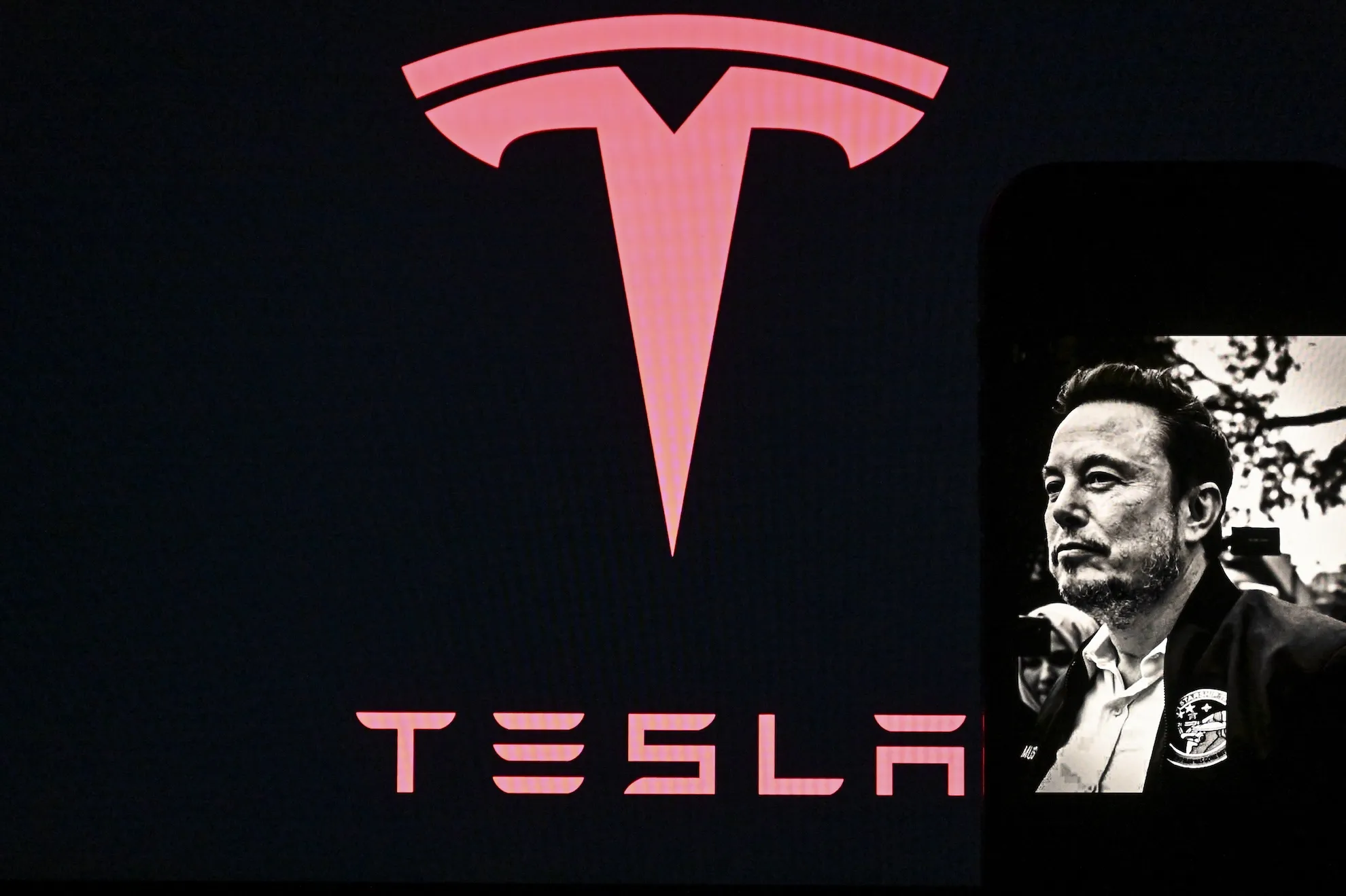Large red Tesla emblem and wordmark beside a black-and-white portrait of a man in a suit.