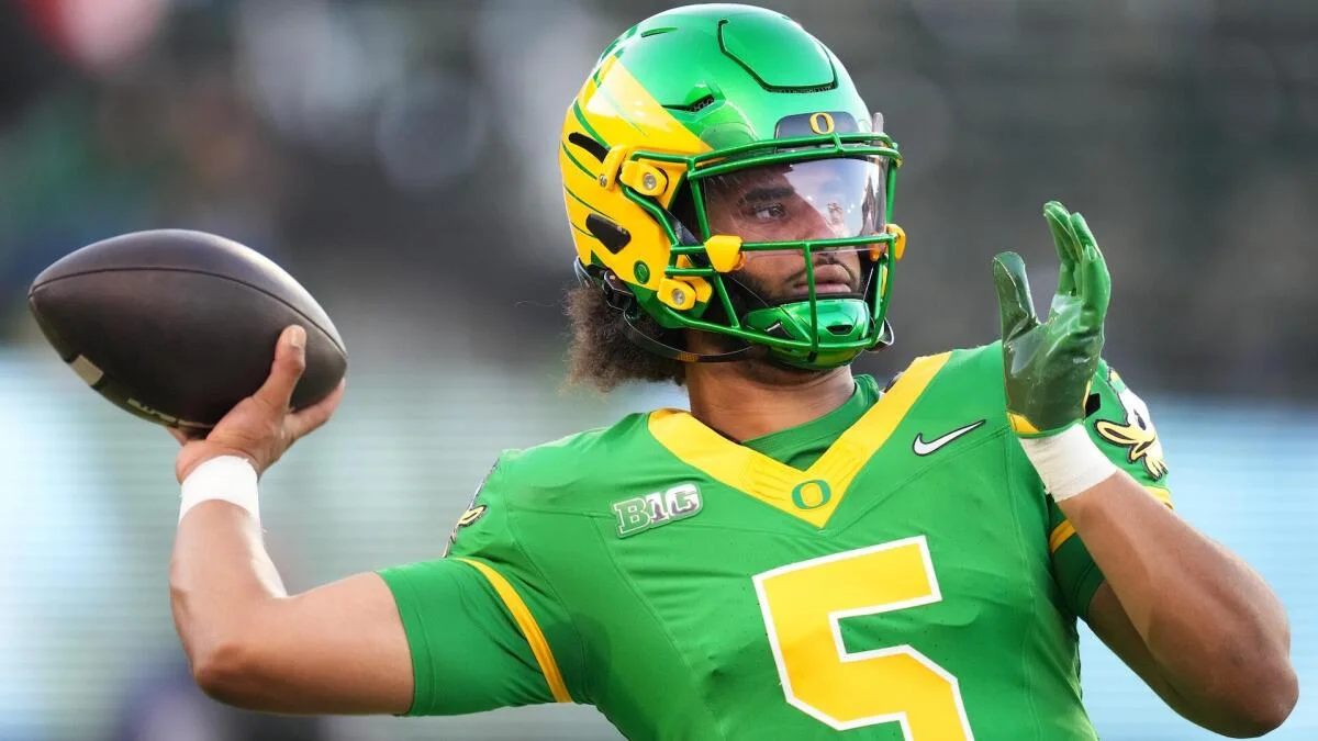 Football player in green and yellow uniform holds a football with one hand raised.