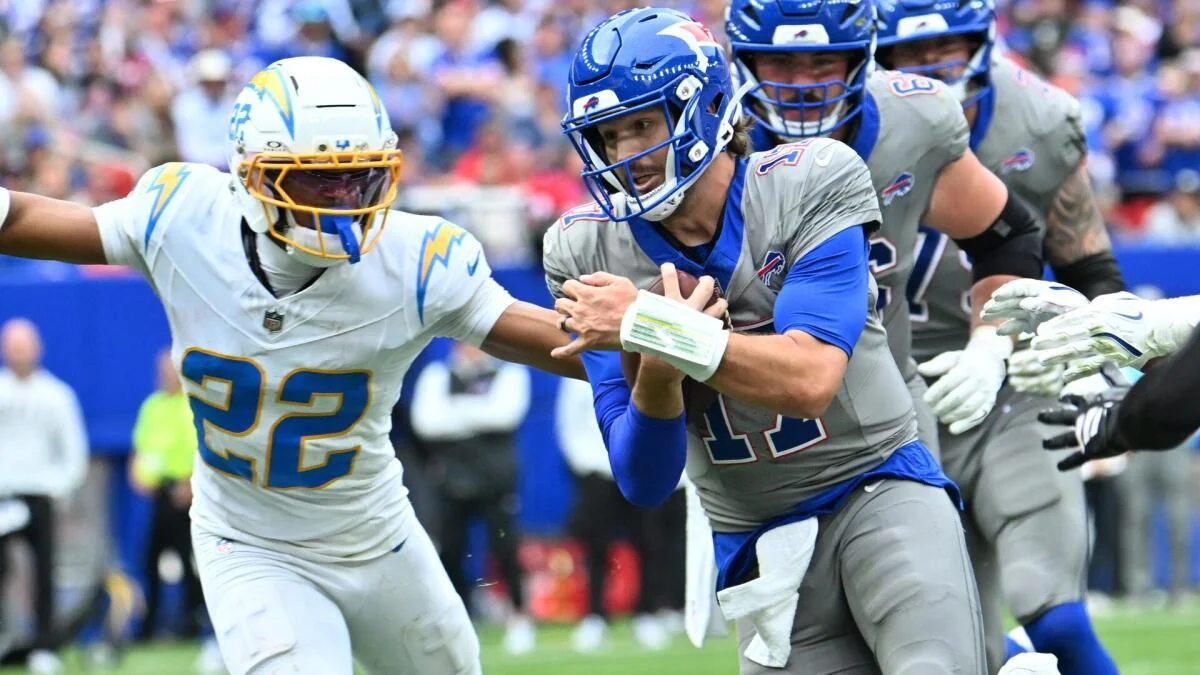 A Bills quarterback clutches the ball as a Chargers defender reaches toward him during a football play.