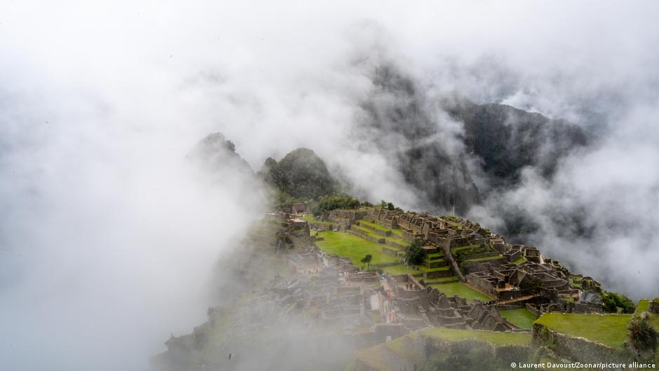 Clouds drift across stone ruins and green terraces on a steep mountain ridge.