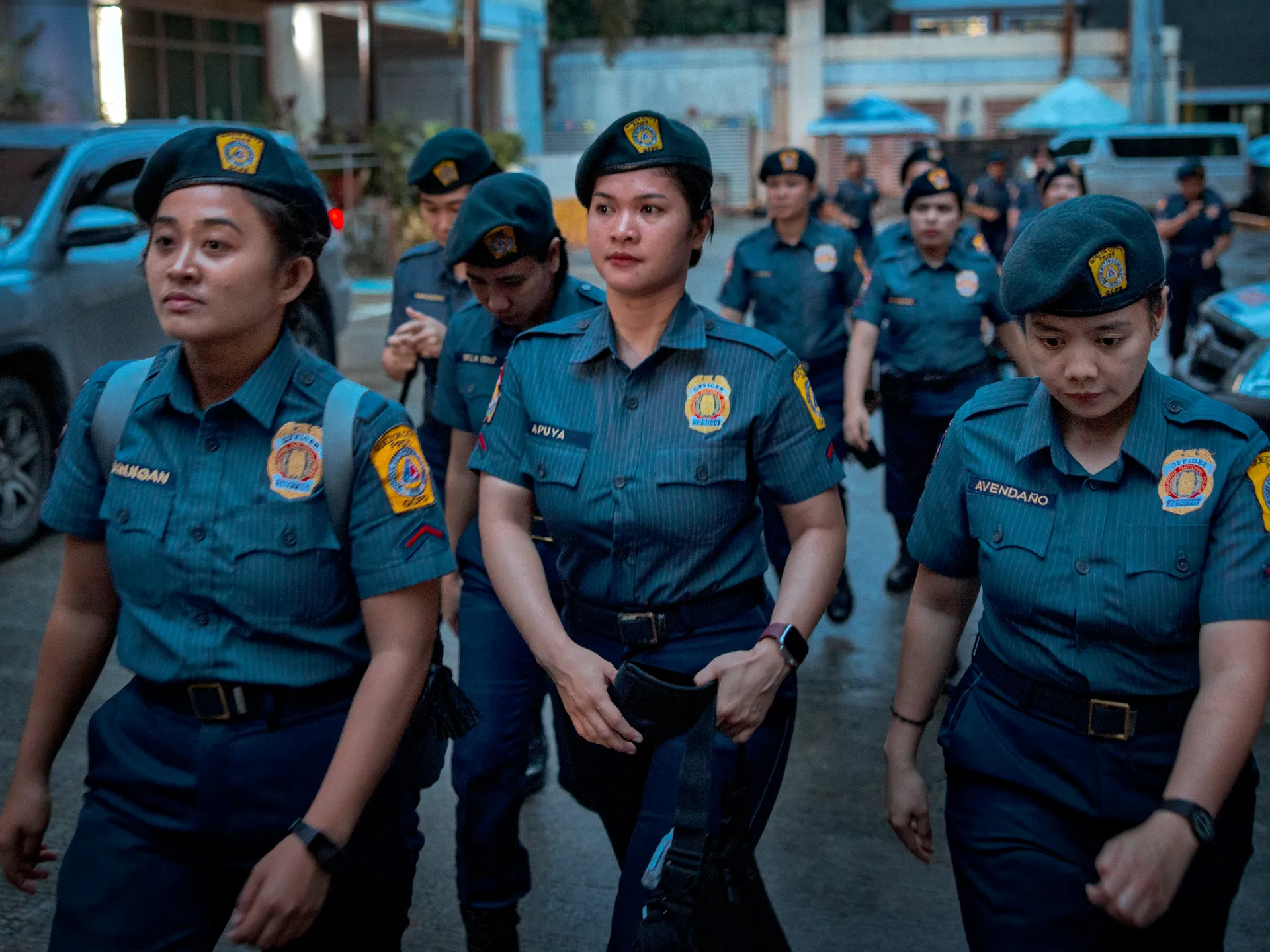 Uniformed women walk in front of several uniformed colleagues on a city street.