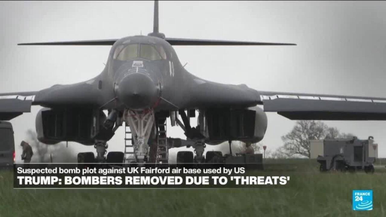 A military bomber is parked on a grassy airfield, with ground equipment and a person nearby.