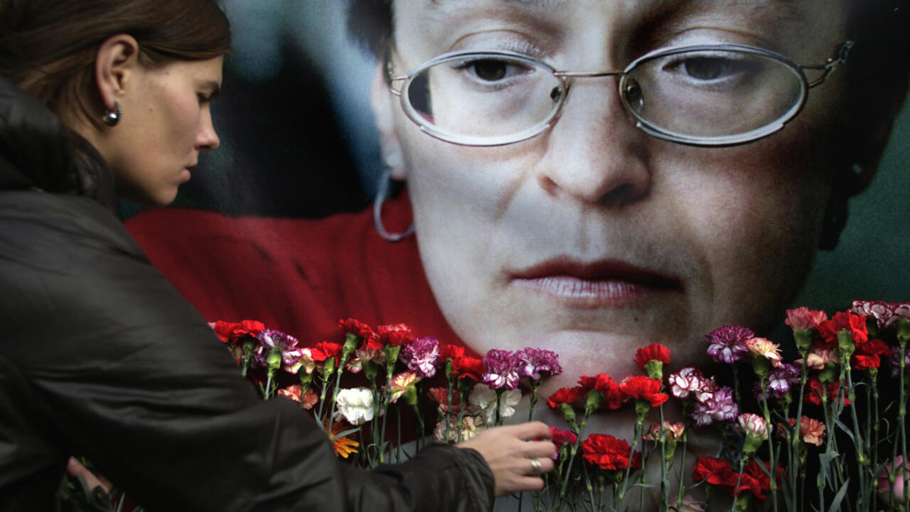 A woman places flowers before a large portrait of a bespectacled woman.