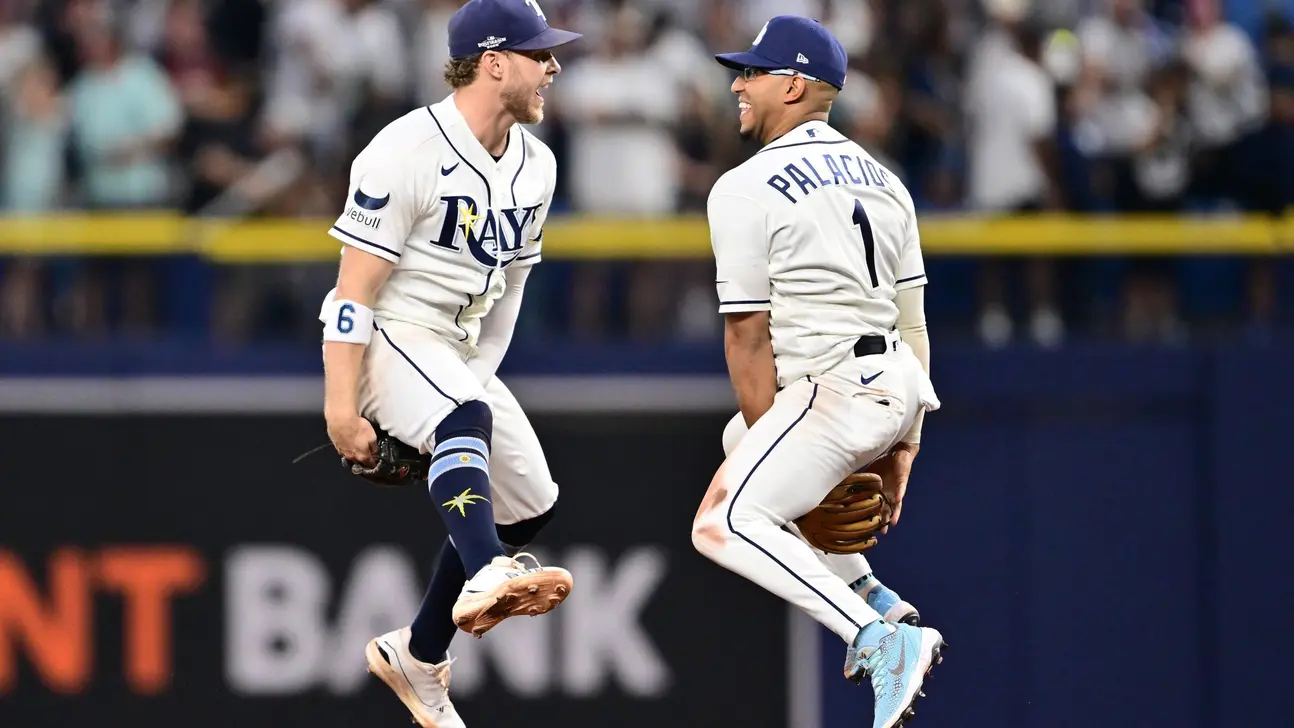 Two Tampa Bay Rays players in white uniforms leap toward each other during a game.