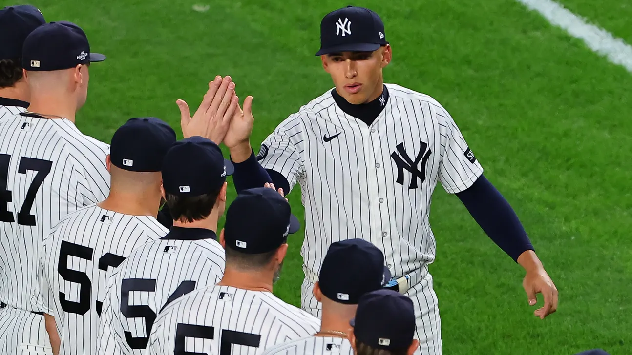Yankees players in pinstriped uniforms high-five on the field during a game.