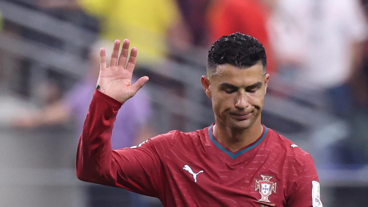 A footballer in Portugal’s red kit raises one hand with his eyes closed.