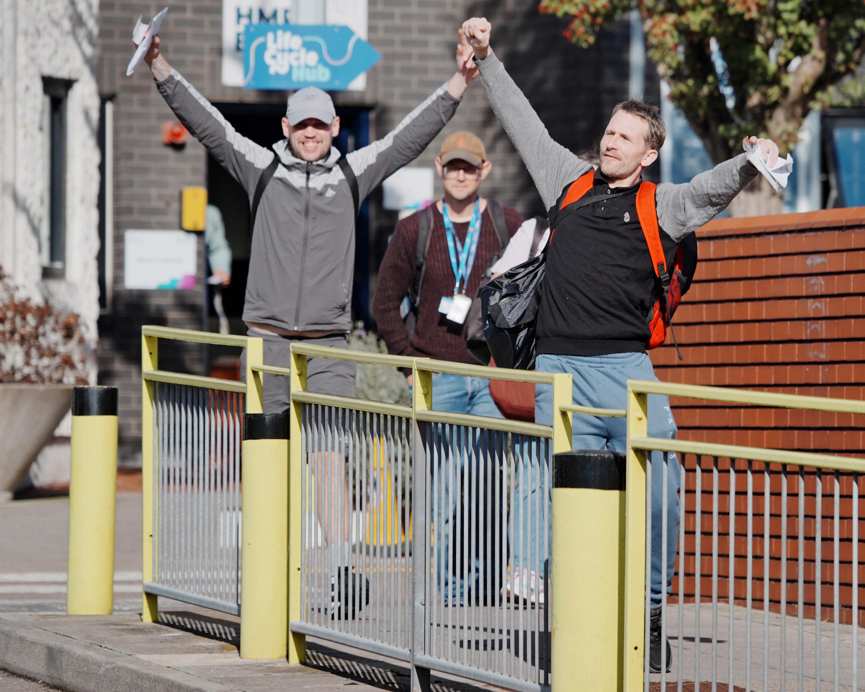Two men raise their arms beside a pedestrian railing, with a third man standing behind them.