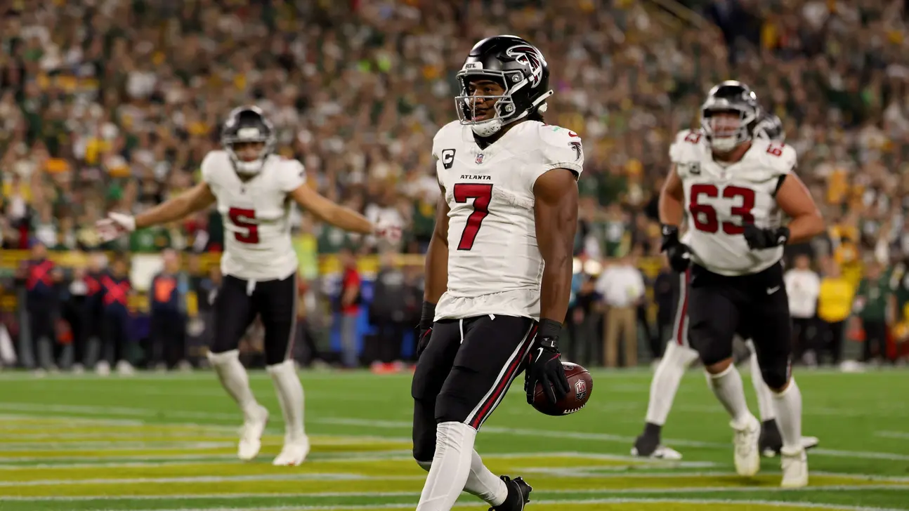 Atlanta Falcons player wearing number 7 walks with a football as teammates stand behind him on the field.