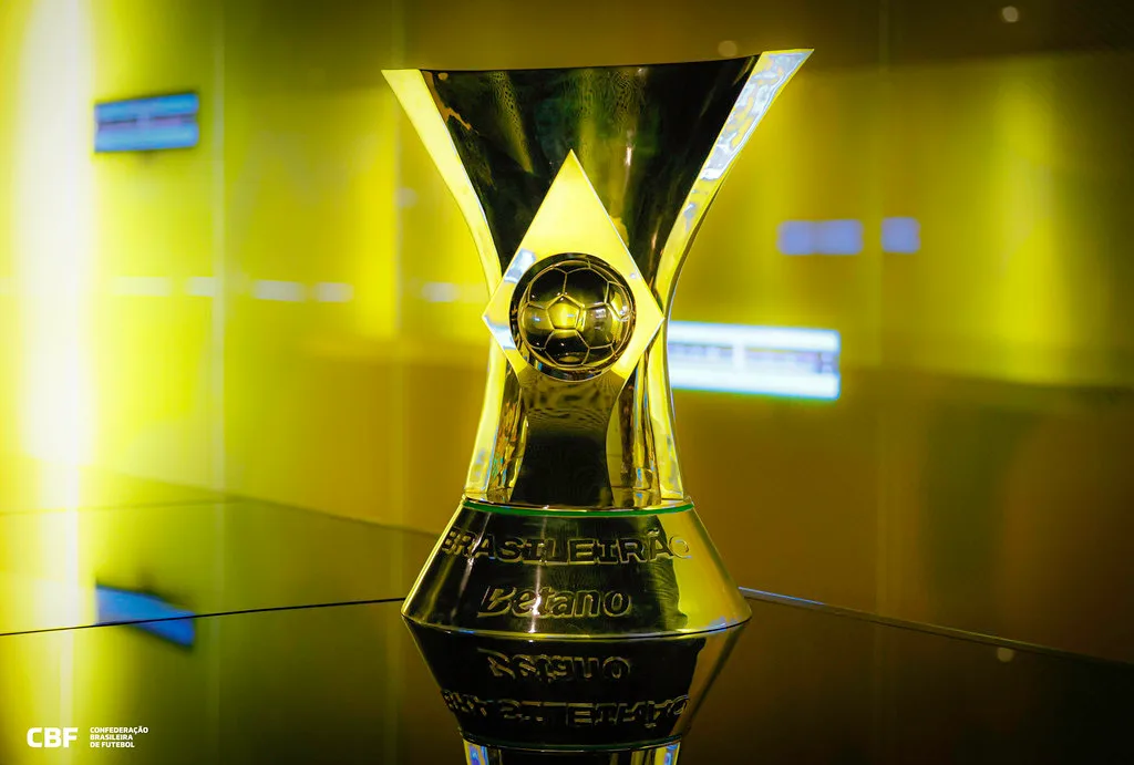 A gold-and-black football trophy stands on a reflective surface in a brightly lit display case.