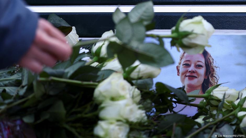 White roses lie across a framed portrait of a woman as a hand places more flowers nearby.