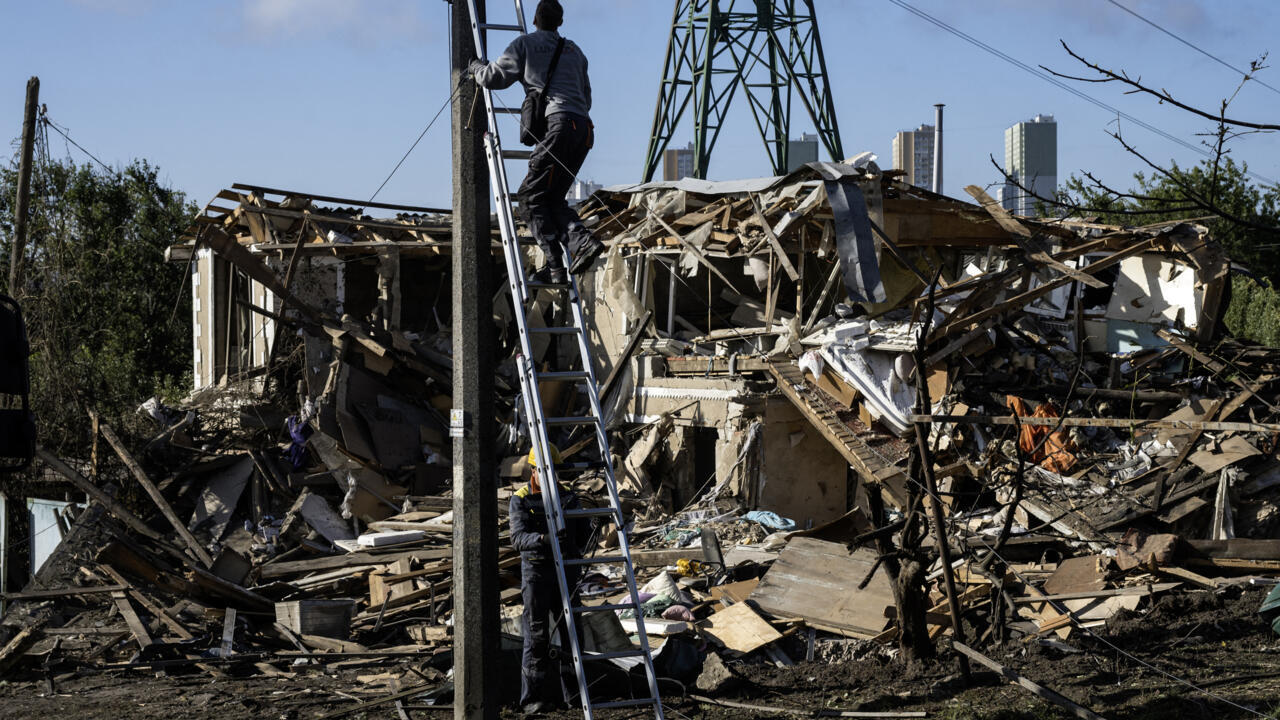 A worker climbs a ladder beside a utility pole amid the rubble of a destroyed building.