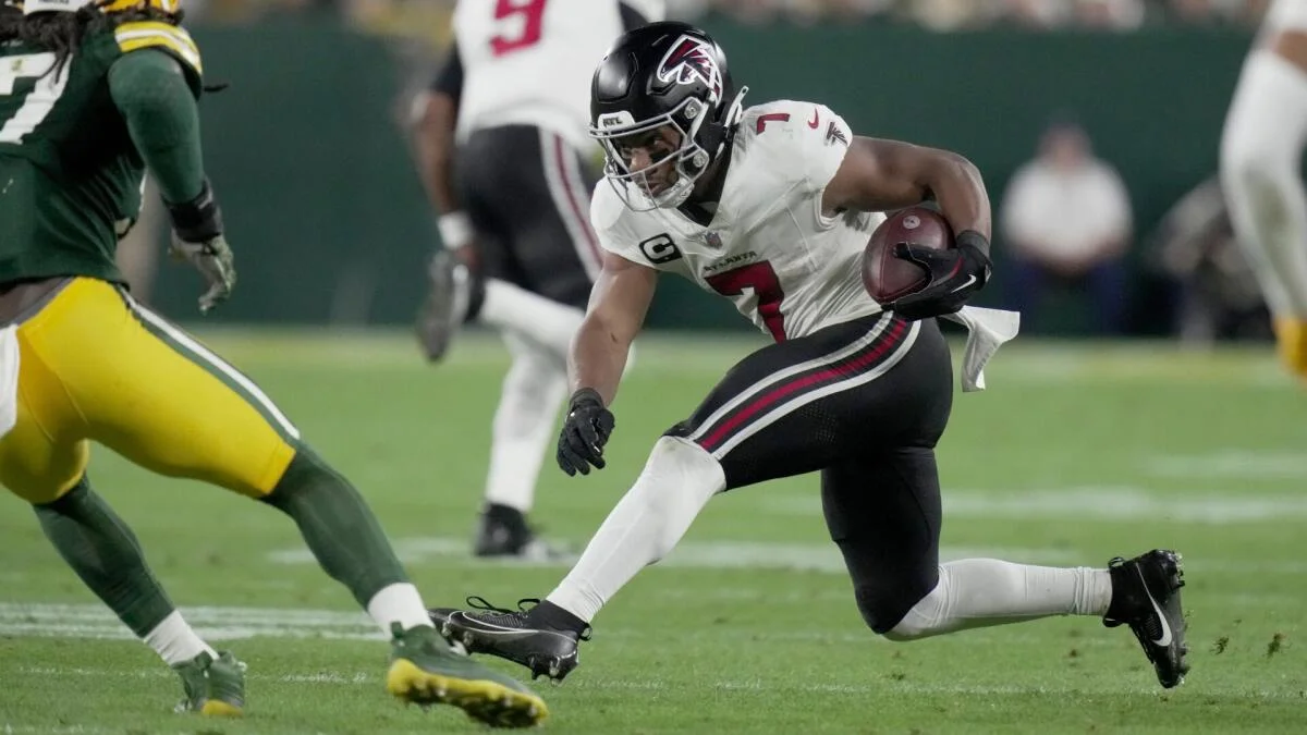 Atlanta Falcons player in white carries the ball as a Green Bay Packers defender approaches.