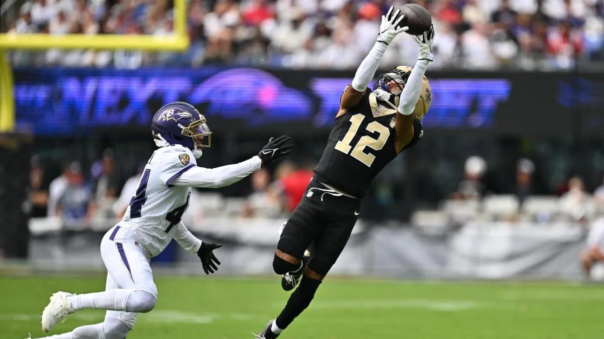 Saints player number 12 catches a football above a Ravens defender during a game.