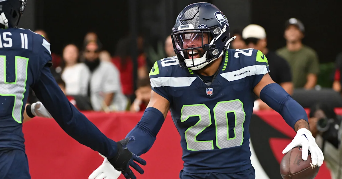 Seattle Seahawks player in number 20 jersey celebrates while holding a football and reaching toward a teammate.