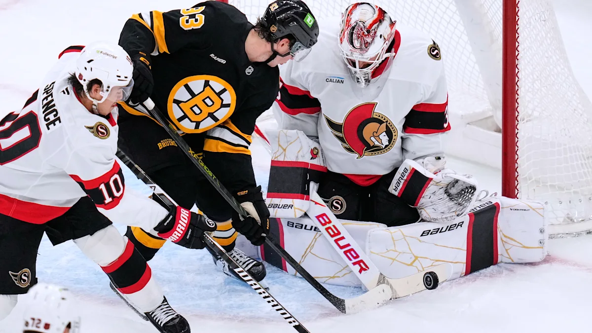 Bruins forward and Senators players crowd the crease as the goalie sprawls beside the net.