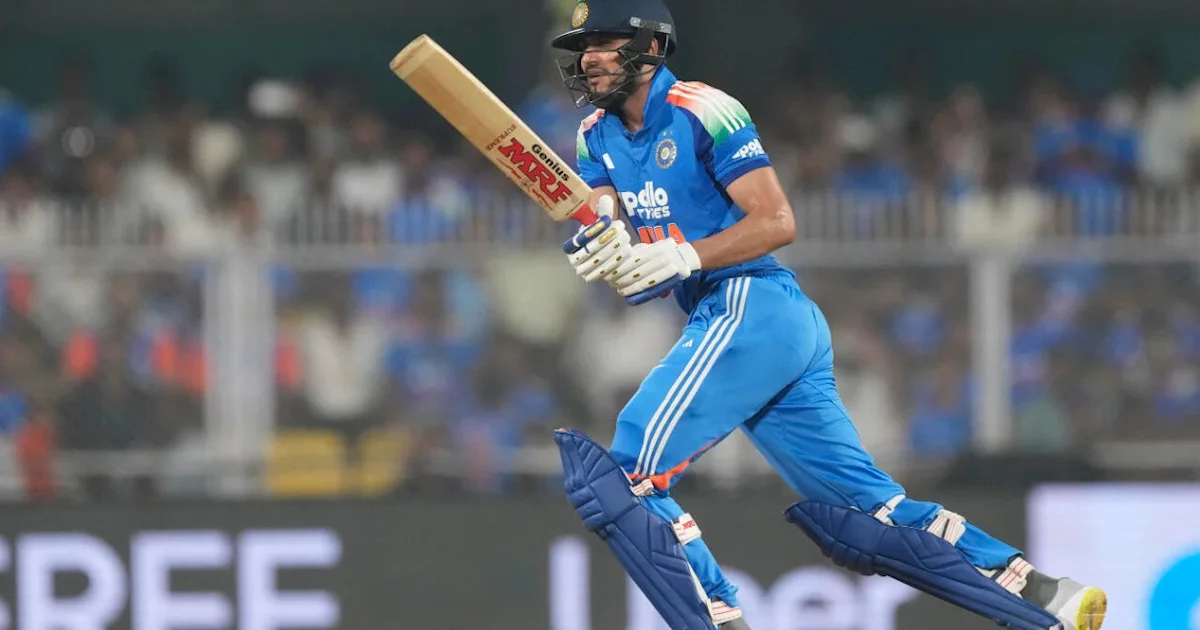 Indian cricketer in blue kit and helmet runs with a bat across a stadium field.