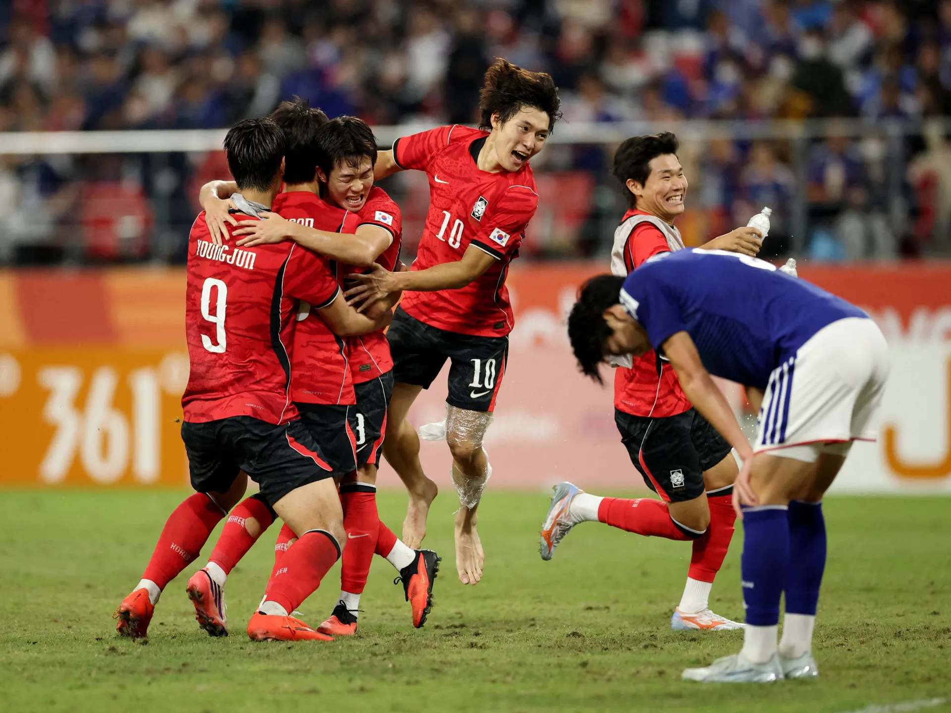 South Korean players in red celebrate together as an opposing player in blue bends forward nearby.
