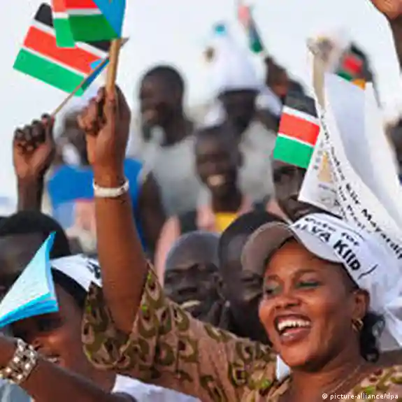 A smiling woman raises a flag as people gather behind her holding flags and signs.